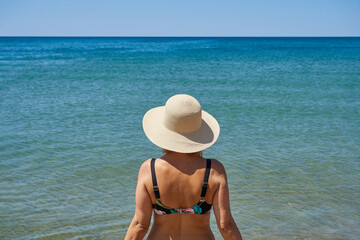 Close-up rear view of a mature woman standing by the sea. Concept of relaxation, travel.