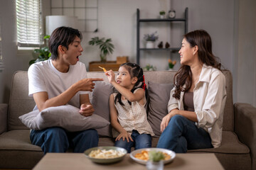 Asian family enjoying snack time on living room couch