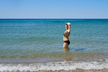 A retired woman in a swimsuit and hat enjoys the sea and sun
