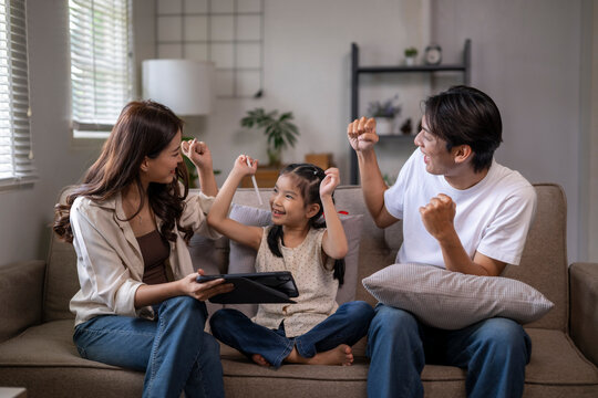 Asian family celebrating success playing game on tablet - Powered by Adobe