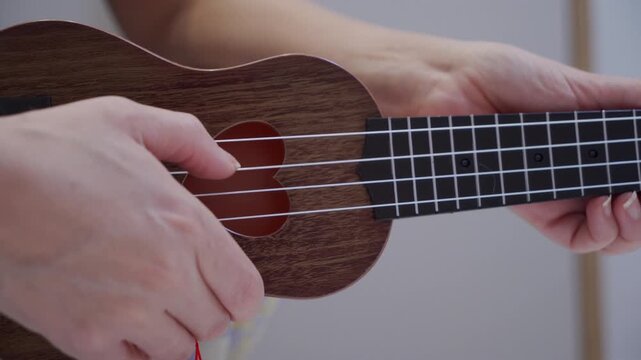 A finger plucks a nylon string on a wooden ukulele. The stringed instrument emits a brief, light single note.