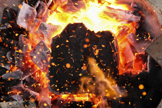 Close up of hot bonfire with burning charcoal, glowing red embers, and bright orange flame. intense heat and powerful energy create dangerous and fiery background