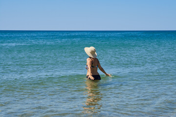 Mature woman wearing a hat and a swimsuit enters the sea with her arms outstretched to swim