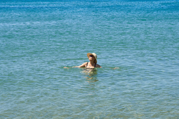 Happy middle-aged woman in a hat swimming in the sea, summer vacation concept