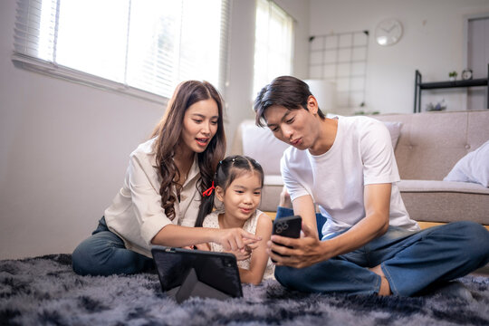 Asian family using digital devices together in living room - Powered by Adobe