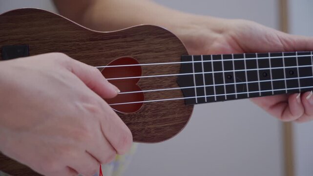 A finger plucks a nylon string on a wooden ukulele. The stringed instrument emits a brief, light single note.