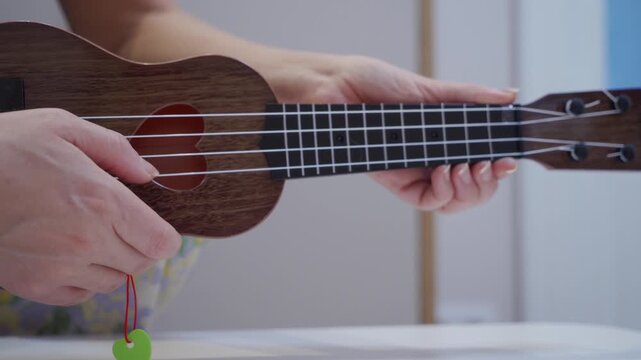 A finger plucks a nylon string on a wooden ukulele. The stringed instrument emits a brief, light single note.