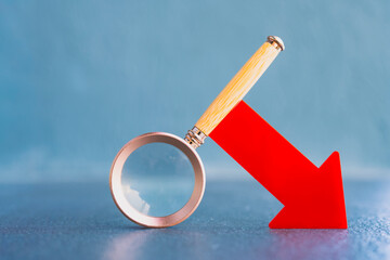 Magnifying glass examining red downward arrow symbolizing data analysis, financial loss, business decline, market downturn, or search for negative performance and economic problems.