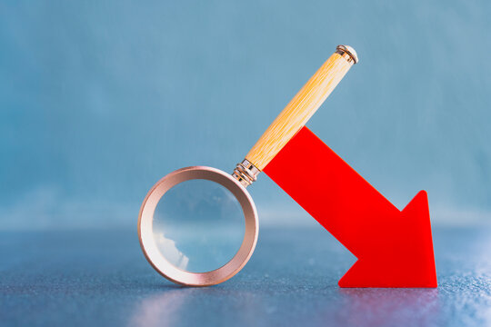 Magnifying glass examining red downward arrow symbolizing data analysis, financial loss, business decline, market downturn, or search for negative performance and economic problems.