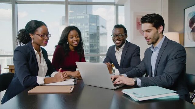 Diverse group of office co workers talking and working together on a project from a laptop in a beautiful white office background on a bright sunny day