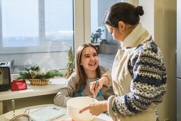 Happy girl with flour on her face laughing with her mother while they mix dough for Christmas cake.