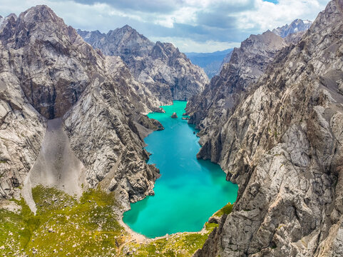 Stunning wide aerial view of a bright turquoise glacial lake flowing through a rocky gorge surrounded by imposing, towering mountain walls