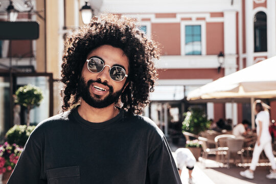 Handsome smiling hipster  model. Sexy unshaven Arabian man dressed in summer clothes. Fashion male with long curly hairstyle posing in the street at sunset. Cheerful and happy. In sunglasses - Powered by Adobe