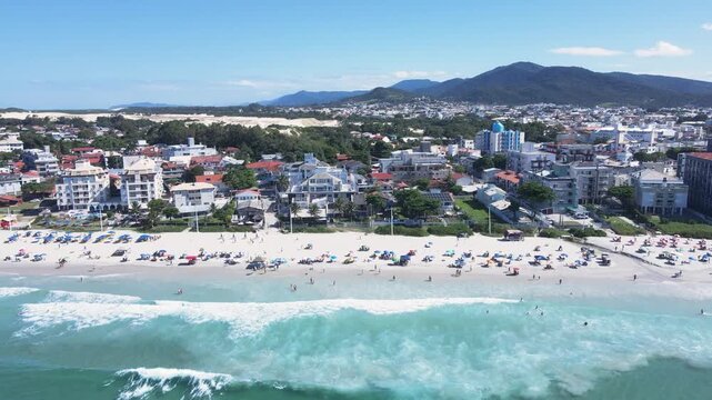 Panoramic aerial view of Ingleses beach in Florian&oacute;polis, Santa Catarina, crowded with people and umbrellas during the peak summer season with turquoise blue sea.