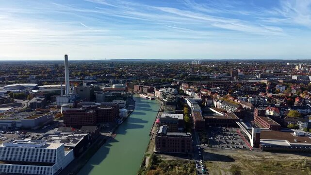 River flowing through German city of M&uuml;nster during sunny day. Modern buildings and houses in German town. Blue sky and colored trees in autumn season. Wide shot. Drone flight.