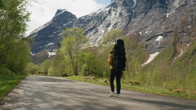 Woman walks along a mountain trail carrying her child in a hiking backpack. Beautiful Norwegian scenery, motherhood and outdoor lifestyle concept.