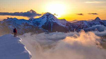 Hiker At Snowy Mountain Peak During Sunset Over Cloudy Valleys in BC, Canada