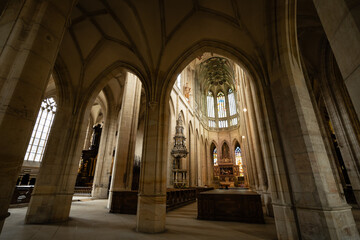 Fototapeta premium Kutná Hora, Czech Republic – August 8, 2025: Side aisle view of St. Barbara’s Cathedral with Gothic arches framing the ornate Baroque altar and chancel in Kutná Hora