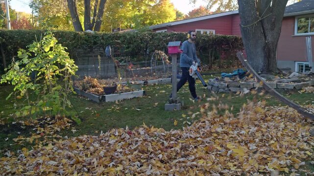 Man in backyard blows a scattering of leaves with a gas leaf blower