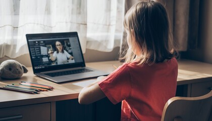 Young girl watching online lesson on laptop at wooden desk with colored pencils, concept for distance learning, online education and home schooling