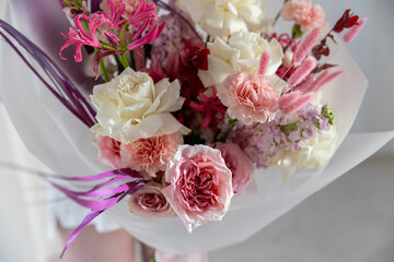 Detailed close-up shot of a magnificent mixed bouquet with lush white and pink roses, carnations, and long purple-pink decorative leaves