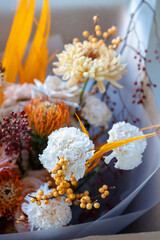 Autumnal floral arrangement featuring peach roses, yellow chrysanthemums, protea, and orange accents, neatly packaged in a brown craft box by a window