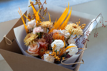 Beautifully arranged autumnal bouquet with peach roses, yellow chrysanthemums, and exotic orange plumes placed in a cardboard delivery box