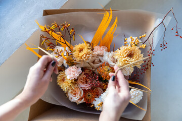 Florist carefully adjusts the elements of a vibrant autumn bouquet, featuring roses and chrysanthemums, inside a craft delivery box