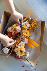 Hands of a florist adding final natural decorative elements to a gorgeous autumnal bouquet in shades of peach, orange, and white