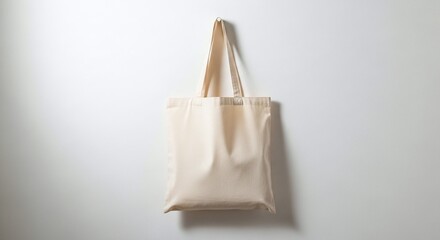 A simple canvas tote bag hanging against a plain white wall in a minimalist studio setting showing shadows