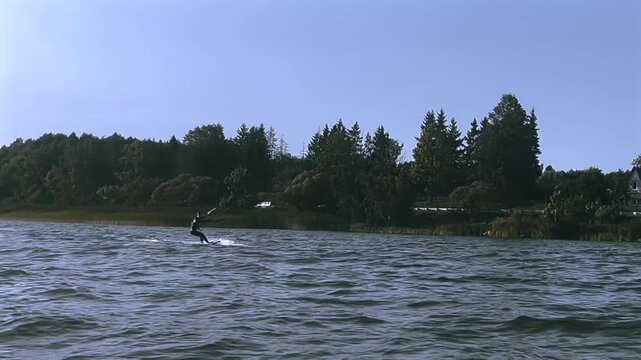 Kitesurfer gliding across the water with trees in the background