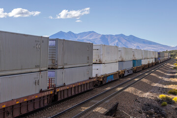 Obraz premium A long container train recedes into the distance towards mountains