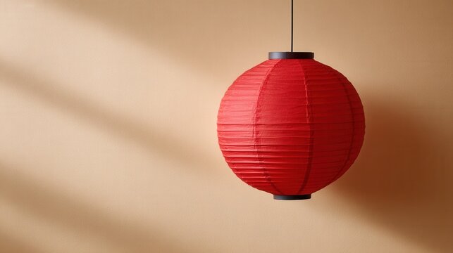A vibrant red paper lantern suspended from the ceiling, casting soft shadows on a beige wall, creating a warm and inviting atmosphere.