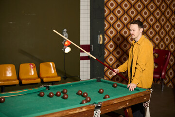 Man plays billiards in retro-style room with striped wall