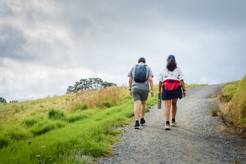 Obraz premium Couple walking uphill under a stormy sky. Long Bay coastal Okura Track. Auckland.