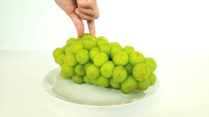 an asian woman's hand holding one sweet green shine muscat grape on a round white plate, isolated on a white background