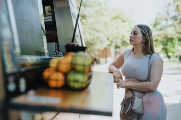 A woman with a handbag waits near a food truck while the atmosphere reflects a calm and sunny day in the park
