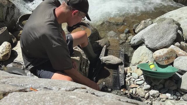 Outdoor adventures on river. Gold panning in a mountain creek, search for gold in summer. Man is looking for gold with a sluice box