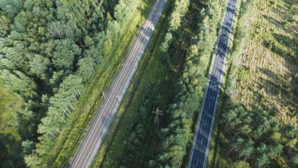 Fotobehang Bospad Overhead view of railway and road through a green forest  © AlexGo