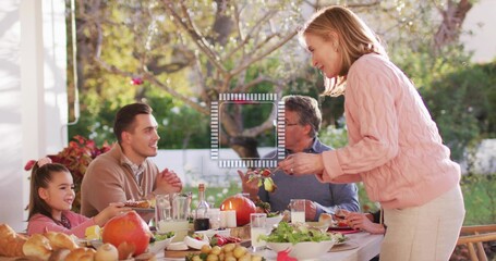 Serving pink-sweatered woman passing dish on covered porch with dining table, man in brown sweater