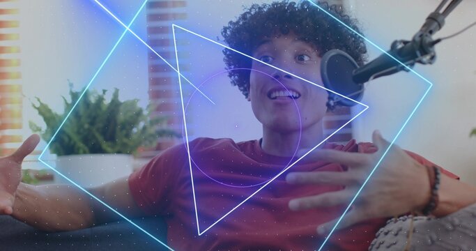 Smiling man in red tee gesturing, speaking to pop-filtered mic on sofa at home, neon overlay - Powered by Adobe