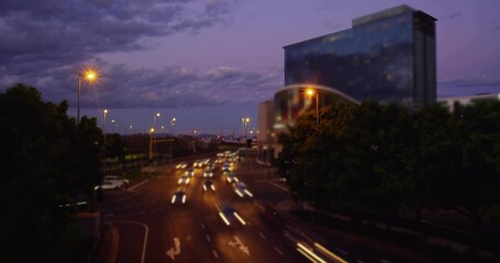 Showing multi-lane roadway with moving cars and light trails from bridge at dusk, with glass tower