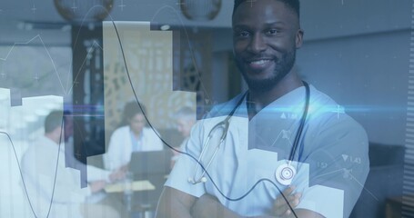 Smiling doctor in blue scrubs standing arms crossed at clinic with stethoscope, laptops, copy space