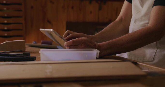 Consulting senior woman in apron using tablet at workbench with plastic container, copy space - Powered by Adobe