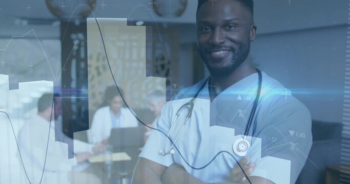 Smiling doctor in blue scrubs standing arms crossed at clinic with stethoscope, laptops, copy space