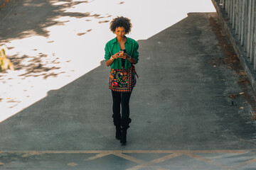 woman with afro hair and mobile phone walking down the street © carballo