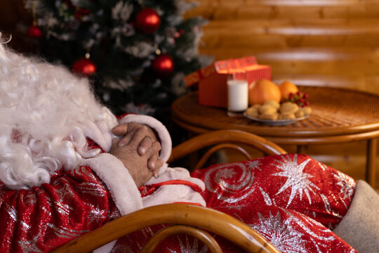 Santa Claus snoozing in a chair next to a festive Christmas tree