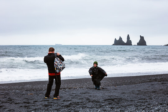 Man taking a photo of child at the beach, Vik, Iceland