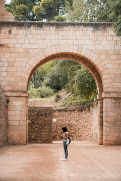 Woman stands under historic arch using phone in old fortress