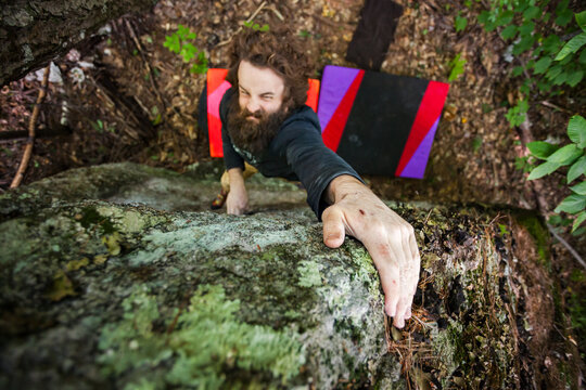 Looking down at a climber reaching the top of a boulder problem